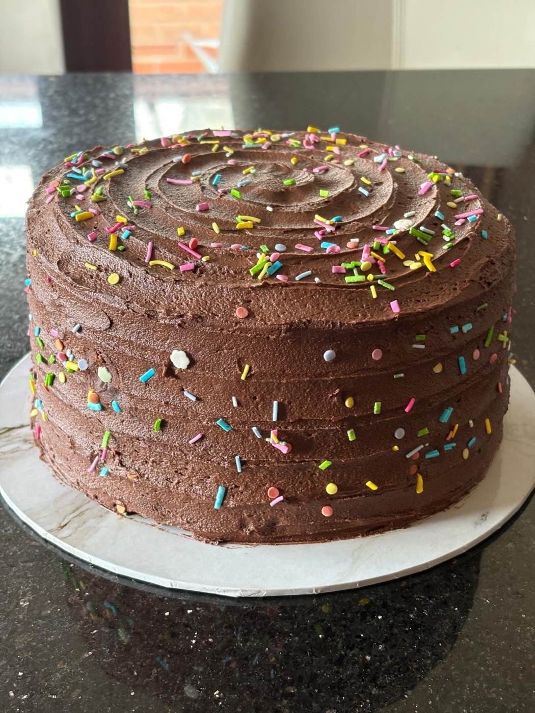Tall chocolate buttercream cake covered in rainbow sprinkles