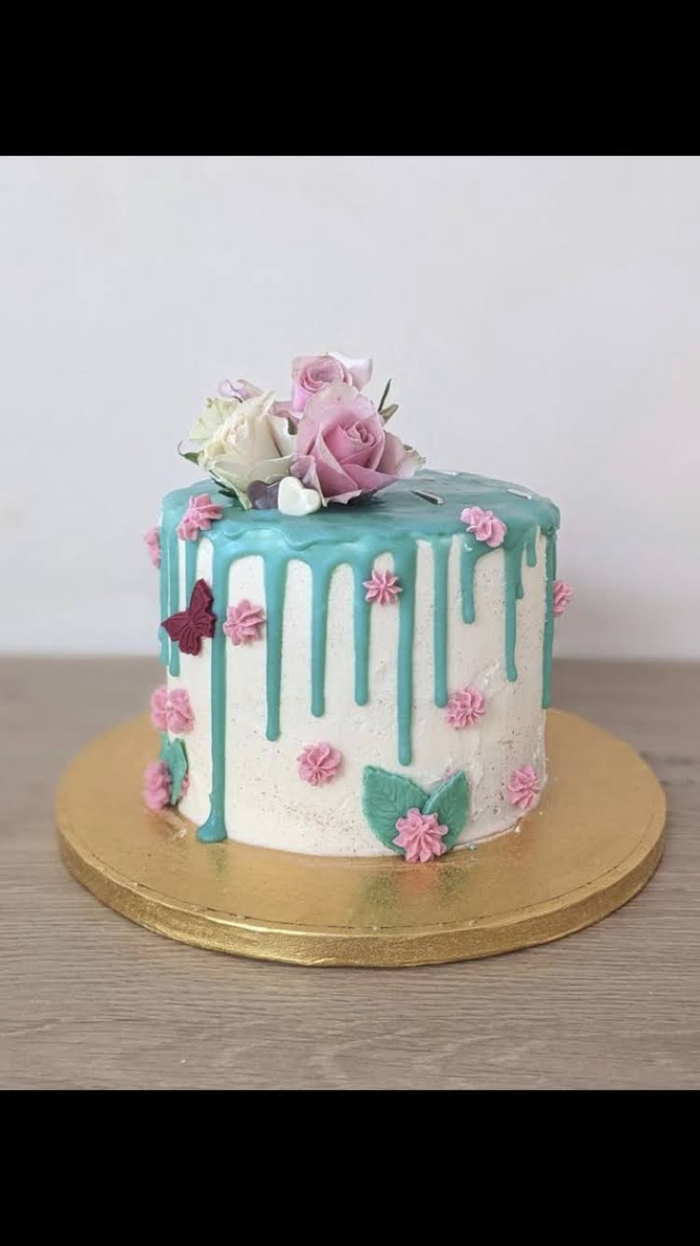 Pastel drip cake topped with real roses, butterflies, and pink piping details