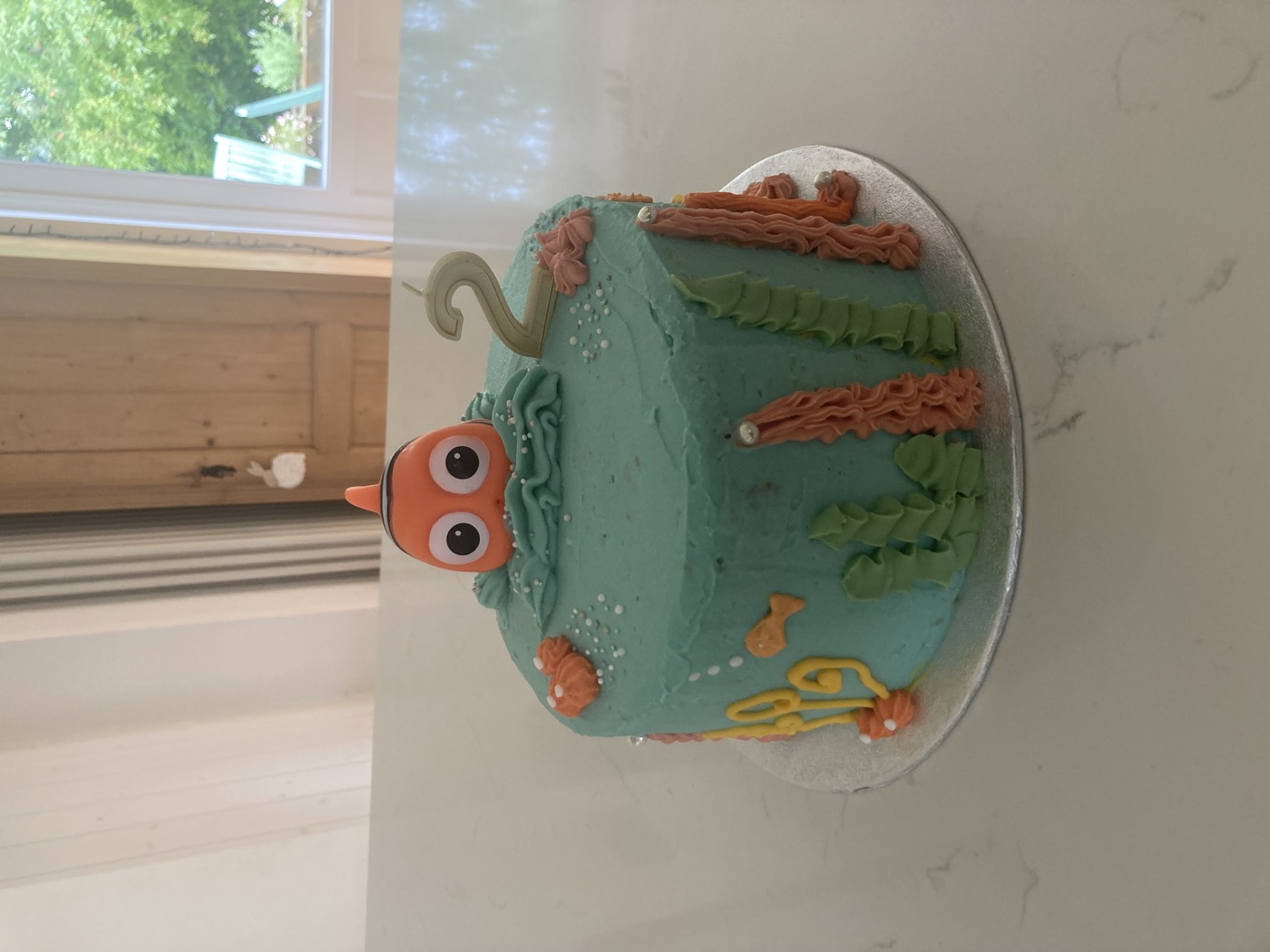 Turquoise birthday cake with a Nemo topper, seaweed piping, and a number two candle